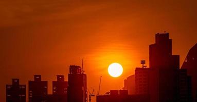 edificio de negocios en el centro al atardecer con un hermoso cielo al atardecer. silueta de condominio y apartamento por la noche. paisaje urbano de rascacielos y grúas de construcción. gran sol con cielo rojo. foto