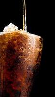 Soft drink pouring to glass with crushed ice cubes isolated on dark background with copy space. There is a drop of water on the transparent glass surface. photo