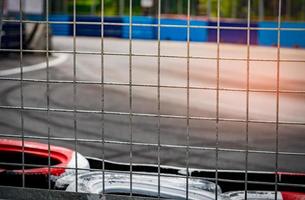 Metal net fence behind tire protection for racing car crash in race track. Red and white tyres safety barrier for racing car. Metal net fence on blurred background of asphalt road car racing circuit photo