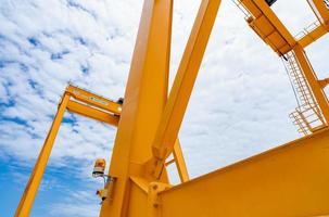 Bottom view of yellow gantry crane against blue sky at port. Gantry crane for cargo and construction industry. Overhead crane for lifting heavy loads. Safety and security working on gantry cranes. photo