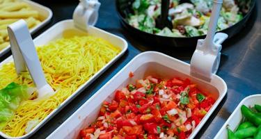 Salad bar buffet at restaurant. Fresh salad bar buffet for lunch or dinner. Healthy food. Chopped tomatoes and yellow noodles in white bowl on counter. Catering food. Banquet service. Vegetarian food. photo