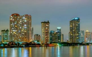 paisaje urbano de edificio moderno cerca del río en la noche. edificio de oficinas de arquitectura moderna. rascacielos con cielo de noche. fotografía nocturna del edificio frente al río. condominio luz abierta en la noche. foto