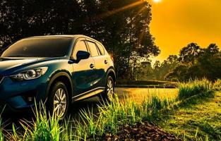 Blue compact SUV car with sport and modern design parked on concrete road at sunrise with orange sky. Environmentally friendly technology. Business success and travel concept. photo