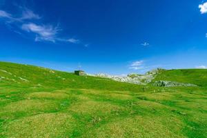 paisaje de hierba verde y colina rocosa en primavera con hermoso cielo azul y nubes blancas. campo o vista rural. fondo de naturaleza en un día soleado. ambiente de aire fresco. piedra en la montaña. foto