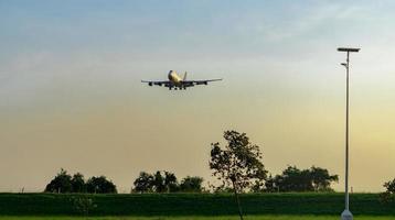 Commercial airline. Passenger plane landing above green trees at airport with beautiful sunset  sky and clouds. Arrival flight. Wire fence and green hedge fence and solar cell panels at the airport. photo