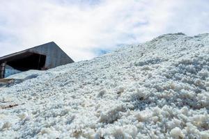 Brine salt farm warehouse with sky and clouds. Pile of organic sea salt. Raw material of salt industrial. Ocean salt. Sodium chloride mineral. Evaporation and crystallization of sea water. Iodine. photo