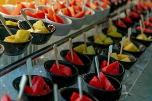 Selective focus tropical fruit buffet at event in restaurant. Catering food. Fresh watermelon and pineapple slices in small bowl on crushed ice on luxury table. Banquet service. Fruit buffet catering. photo