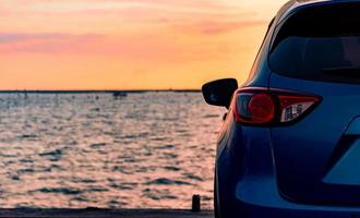 Blue compact SUV car with sport and modern design parked on concrete road by the sea at sunset. Environmentally friendly technology. Electric car technology and business. Hybrid auto and automotive. photo