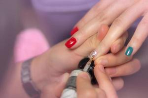 Women receiving fingernail manicure service by professional manicurist at nail salon. Beautician painting nails at nail and spa salon. Focused on white and glitter nail polish at nail salon. photo