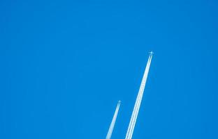 dos aviones con pistas de condensación blancas. avión a reacción en el cielo azul claro con estela de vapor. viajar por concepto de avión. rastros de gases de escape del motor del avión. aviones con rayas blancas. foto