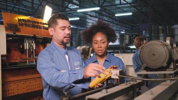 Asian male and female African American engineers in safety uniform work by inspecting machines' voltage current, checking, and maintaining at manufacture factory, electric system service occupations. video