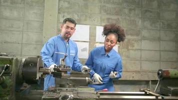 due lavoratori professionisti del settore in uniformi di sicurezza e un partner di ingegneri hanno lavorato con strumenti di precisione per la lavorazione dei metalli e hanno discusso del disegno meccanico per l'officina di macchine per tornio nella fabbrica di produzione. video