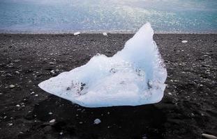 Diamond Beach in Iceland with blue icebergs melting on black sand and ice glistening with sunlight photo