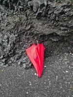 A lone red umbrella on the endless black beaches of Iceland in front of black basalt rock formations. photo