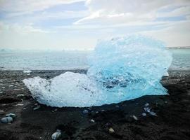 Diamond Beach in Iceland with blue icebergs melting on black sand and ice glistening with sunlight photo