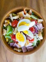 Above view of the fresh organic salad with ham and boiled egg in the wooden bowl. photo