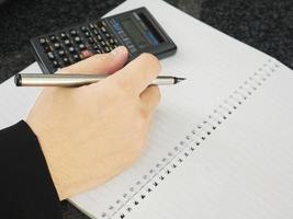 Business man is holding pen with empty note book working with calculator. Financial working concept. photo