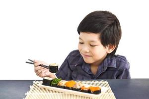 Chico encantador asiático está comiendo sushi sobre fondo blanco. foto