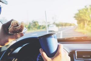 Man is dangerously eating hot dog and cold drink while driving a car photo