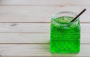 Cold green soda in a big glass over wooden background photo