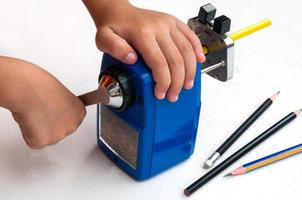 A boy is sharpening his pencil using mechanical sharpener over white background photo