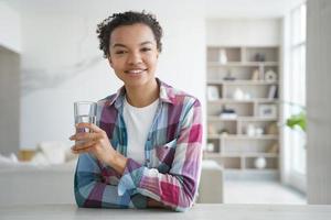 feliz niña afroamericana bebe agua de un vaso. estilo de vida saludable, rutina de salud matutina. foto