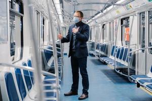 Coronavirus, Covid-19. Sick man feels unwell, has shortage of breathing, wears medical mask, poses in subway carriage, protects from contagious disease, avoids contact with people and viruses photo