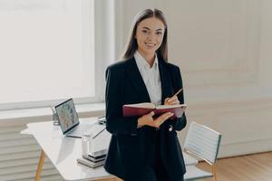 Female director holding notebook and pencil while leaning on office desk photo