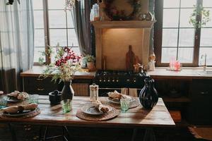 interior de la cocina. mesa de comedor servida con platos vasos decoración floral. cubertería y cristalería. preparación para la cena festiva. arreglo de mesa para cena familiar foto