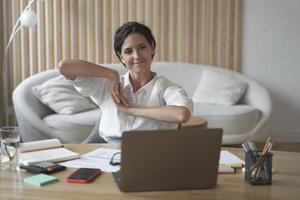 Positive business woman doing hands stretching exercises while listening to training lectures online photo