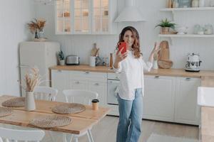 Young hispanic woman boasting with her stylish kitchen. Housewife has video phone call at home. photo