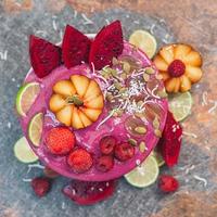 Food and art concept. Beautifully designed fruit. Ice cream with pink pitaya, slices of red dragon fruit, strawberry, raspberry, lime, coconut flakes, pumpkin seeds photo