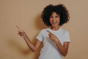 Young african american girl cheerfully smiling and pointing with index fingers up to side photo