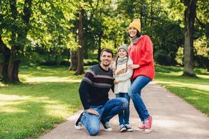 Carefree restful family have walk together, enjoy sunny autumn weather, green beautiful park and fresh air, pose into camera, embrace each other, have model relationship. Joyful child and parents photo