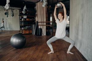 Sportive woman training with small pilates ball in half sitting position during ballet workout photo