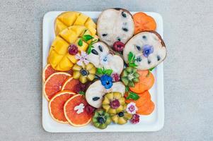 Flat lay of exotic tropical fruits. Gold kiwi, persimone, raspberry, mango, oranges and mint. Plate of fresh decorated craved ripe fruits. Food concept photo