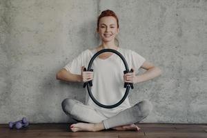 Cheerful fitness woman in active wear sitting in lotus position and exercising with pilates ring photo