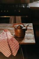Retro aluminium kettle on wooden table with red striped towel near. Copper old teapot uses for making tea. Old fashioned kitchenware photo