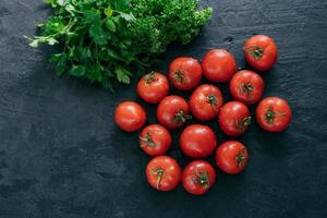 Top view of red ripe fresh tomatoes with green parsley on dark background. Vitamins and nutrition concept. Copy space. Raw food photo