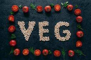 Photo of tomatoes frame and chickpea letters meaning veg. Organic seeds inside of vegetable frame isolated over dark background. Vegeterinarism