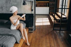 ritual de belleza matutino para el cuidado de la piel. hermosa mujer europea aplicando loción hidratante corporal. foto