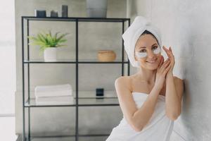 Young happy woman is relaxing at luxurious spa resort. Girl applies anti wrinkle eye patches. photo