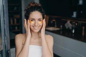 Pretty young lady wrapped in towel after bathing is happy and relaxing applying eye patches. photo