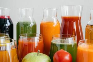 Close up shot of glass bottles filled with colorful juice made of various vegetables and fruit, red tomato and green apple in foreground. Fresh detox drink photo