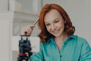 Close up shot of happy redhead woman records video on webcam, talks to subscribers, has personal blog, gives advice, makes live broadcast or fims webinar. Online teacher records vlog teaches languages photo