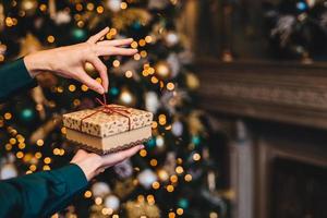 Surprisment and pleasant moments concept. Woman wrapps New Year gift as stands in living room near beautiful decorated fir tree. Holidays, x mas and celebration concept. photo
