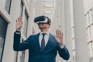 Man in formal blue suit walking around in virtual reality while wearing VR goggles photo