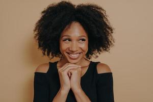 Studio shot of happy Afro girl keeps hands together under chin photo