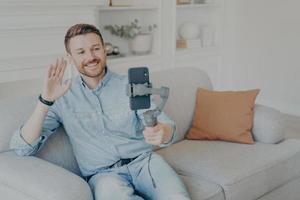 Young man enjoying video chat with family on cellphone while sitting on sofa in living room photo