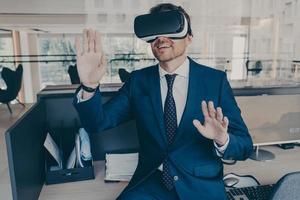 Excited entrepreneur in virtual reality glasses touching objects interact with 3D simulation photo